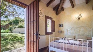 Una camera da letto con una porta in legno, una struttura letto in metallo bianco e vista sul giardino.