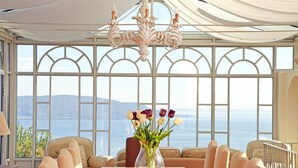 Ein Essbereich mit Tisch, Stühlen, einer Blumenvase und Meerblick durch große Fenster.