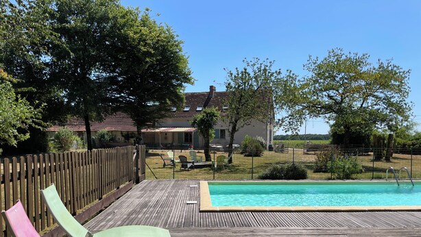 Un terrazzo in legno con poltrona relax, piscina e una casa sullo sfondo.