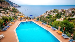 A swimming pool with sun loungers and umbrellas, surrounded by buildings with a view of the sea. - Eden House Positano, Amazing Seeview Apartment Car Parking shared pool (Positano)