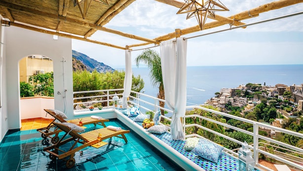 An infinity pool with wooden loungers, a star-shaped light fixture, and a view of a coastal town. - Eden House Positano, Amazing Seeview Apartment Car Parking shared pool (Positano)