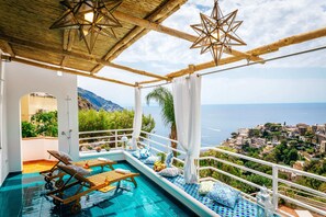 An infinity pool with wooden loungers, a star-shaped light fixture, and a view of a coastal town. - Eden House Positano, Amazing Seeview Apartment Car Parking shared pool (Positano)