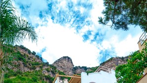 A staircase leading to a white building with a balcony, surrounded by greenery and a mountainous backdrop. - Eden House Positano, Amazing Seeview Apartment Car Parking shared pool (Positano)