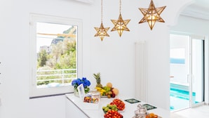 A bright room with a large window, a table with fruits and drinks, and star-shaped hanging lights. - Eden House Positano, Amazing Seeview Apartment Car Parking shared pool (Positano)