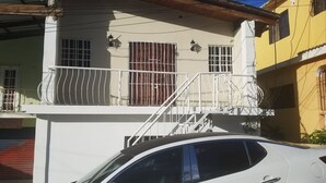 Un edificio de dos pisos con un balcón, una escalera y un coche estacionado en la parte delantera.