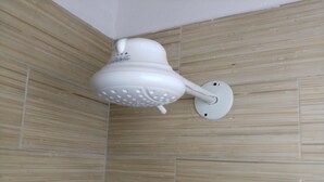 Un cabezal de ducha blanco montado en una pared con un patrón de baldosas beige texturizadas.