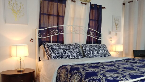 Una cama bien hecha con ropa de cama estampada, una mesita de noche con lámpara y cortinas en la ventana.