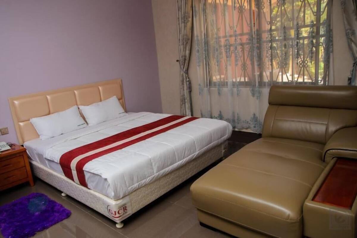 A bedroom with a bed, a sofa, a nightstand, and a window with curtains.
