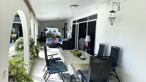 A covered patio with a dining table, chairs, and a fruit basket.
