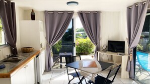 A compact kitchen with a dining area, a TV, and a poolside view.