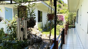 A balcony with potted plants, a small garden area with rocks and a statue, and a tiled floor.
