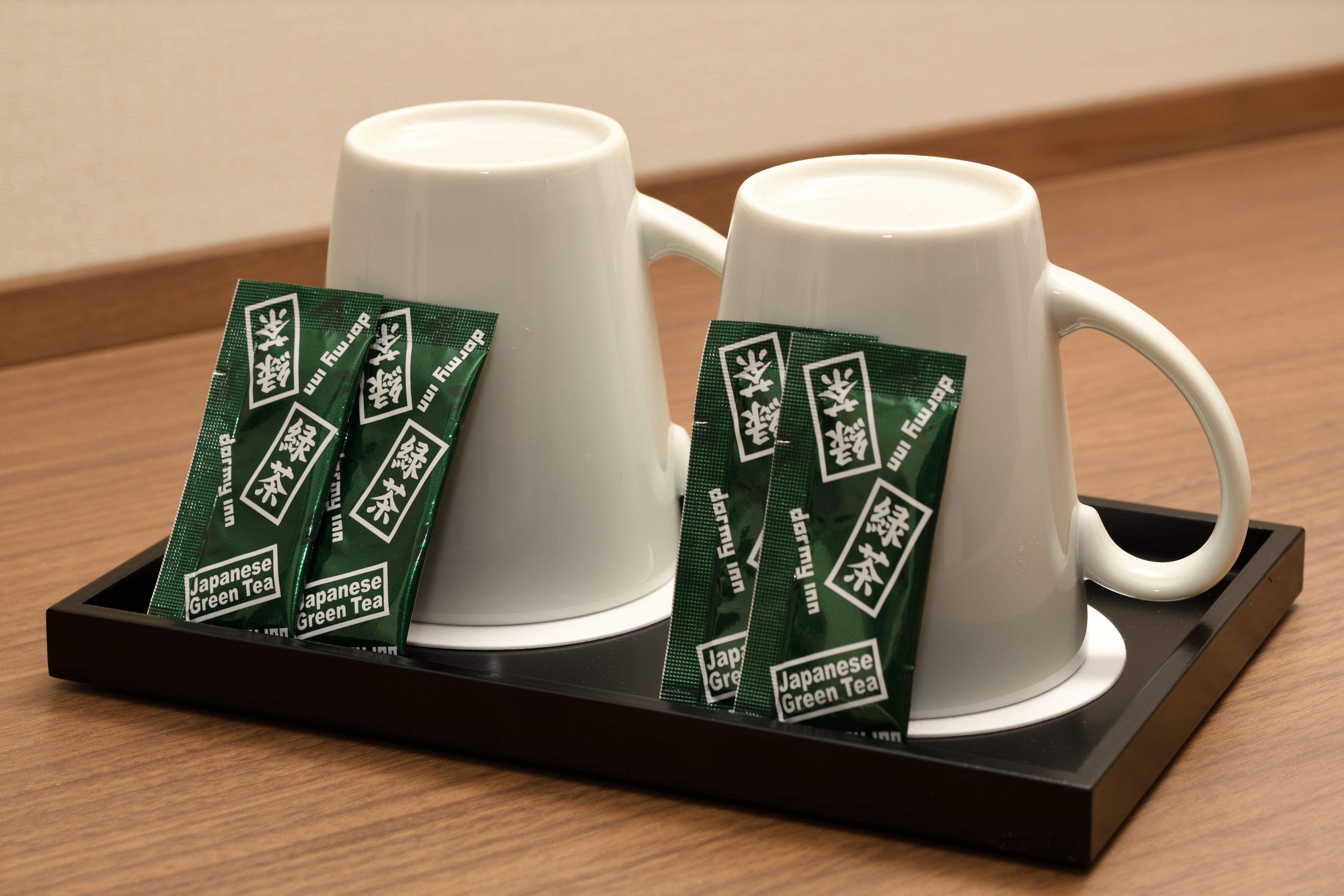 Deux tasses en céramique blanche sur un plateau noir, accompagnées de sachets de thé vert étiquetés « Thé vert japonais ».
