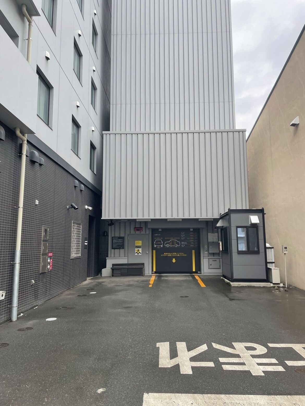 A building entrance with a ramp leading to a door, a bench, and a trash can.