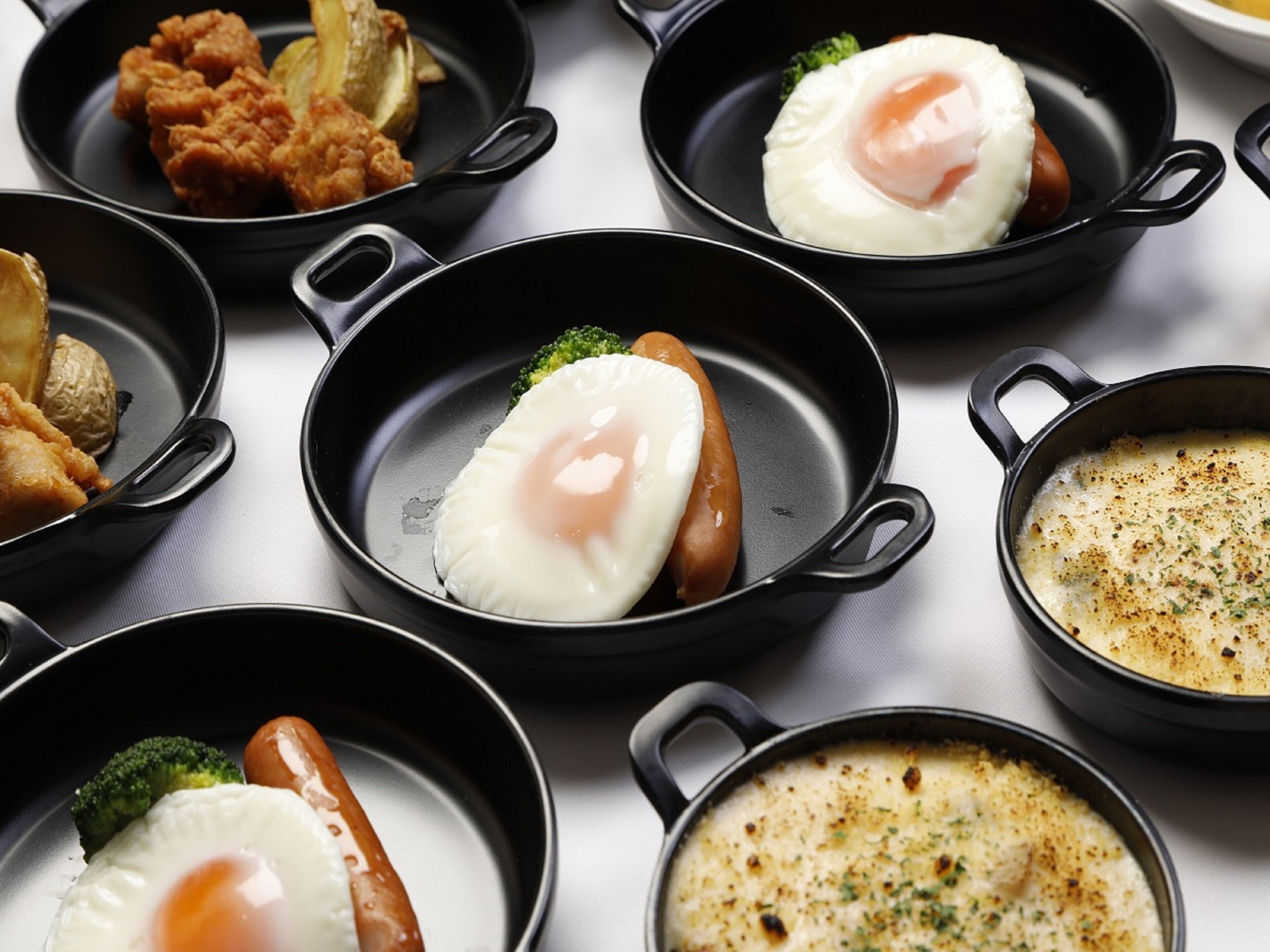 A variety of dishes including fried eggs, sausages, and a creamy soup in black cast iron skillets.