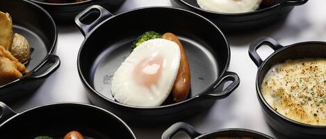 Variedad de platos que incluyen huevos fritos, salchichas y una crema abundante, todo servido en sartenes de hierro fundido negras.