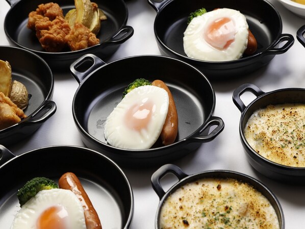 A variety of dishes including fried eggs, sausages, and a creamy soup in black cast iron skillets.