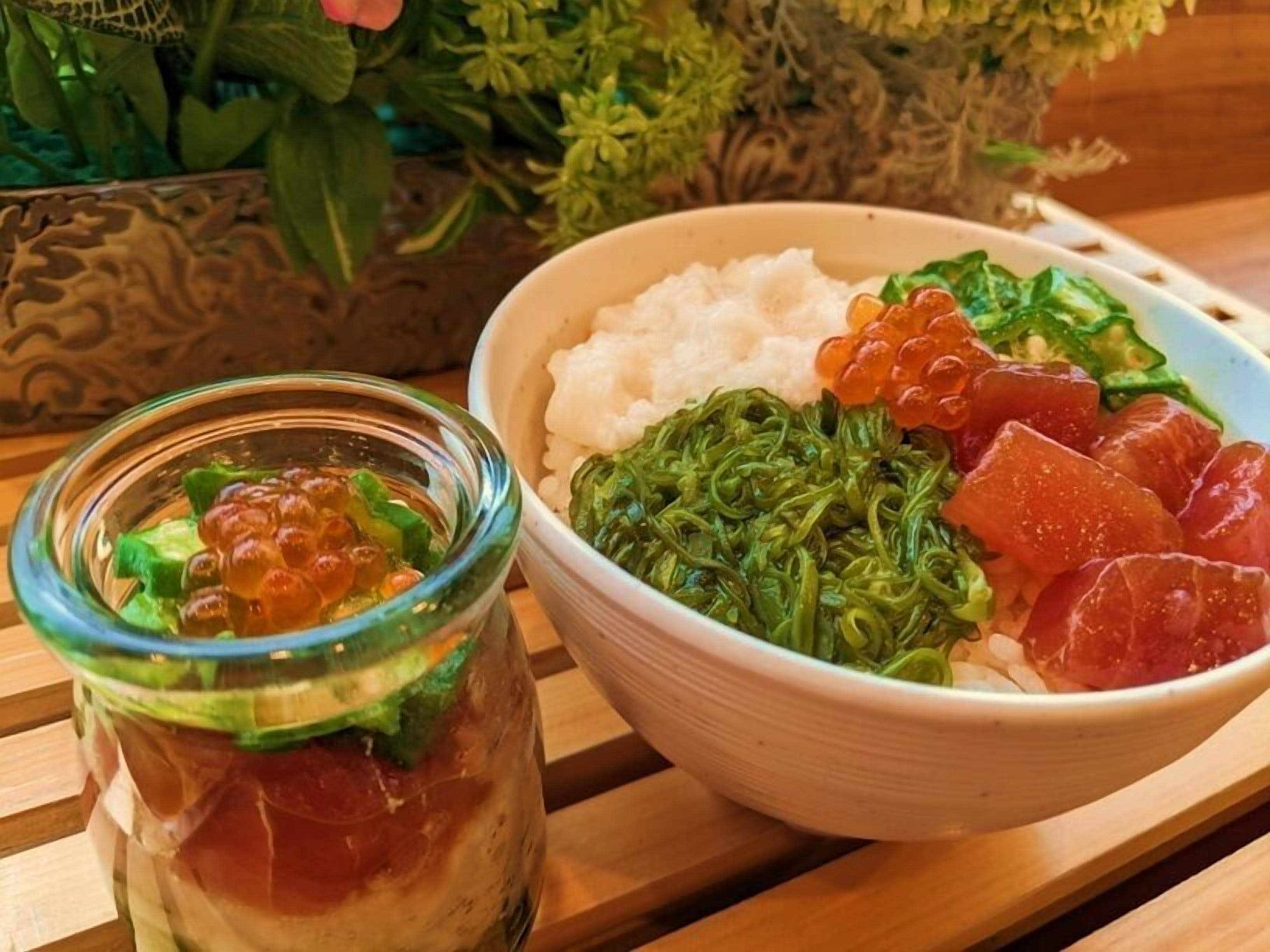 A wooden table with a bowl of rice, seaweed, and fish roe, and a jar of pickled vegetables.