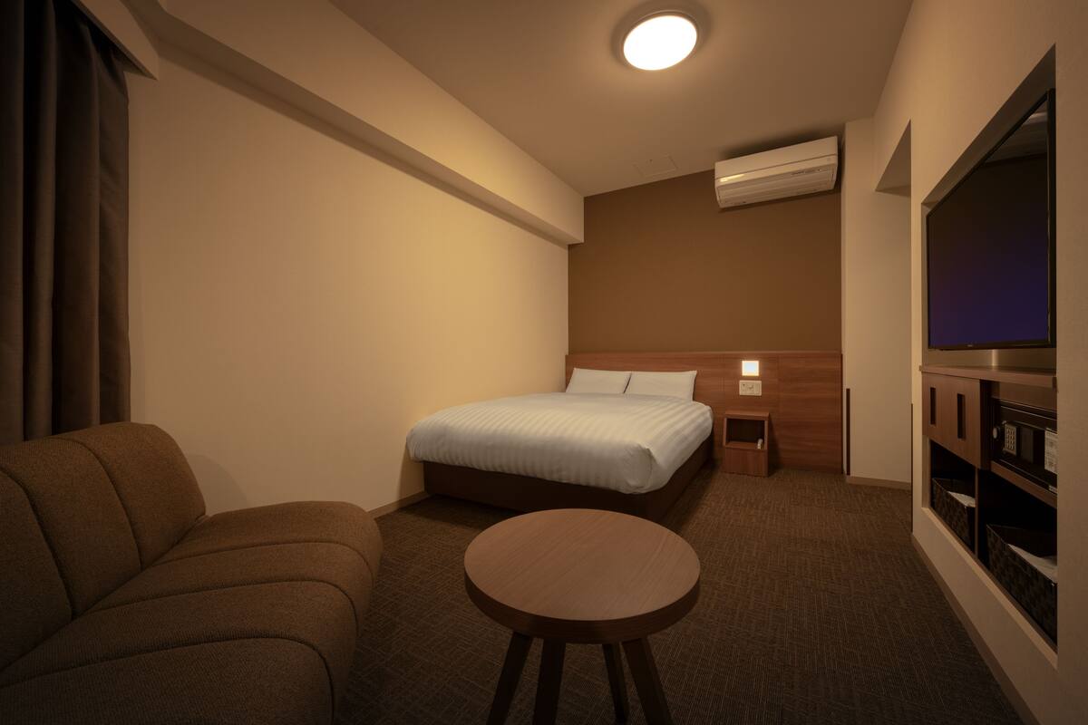 Una habitación de hotel con cama, sofá, una mesita y televisión.
