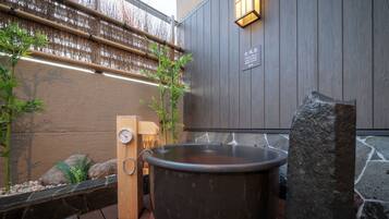 A hot tub in a spa area with wooden benches, bamboo plants, and a stone wall.