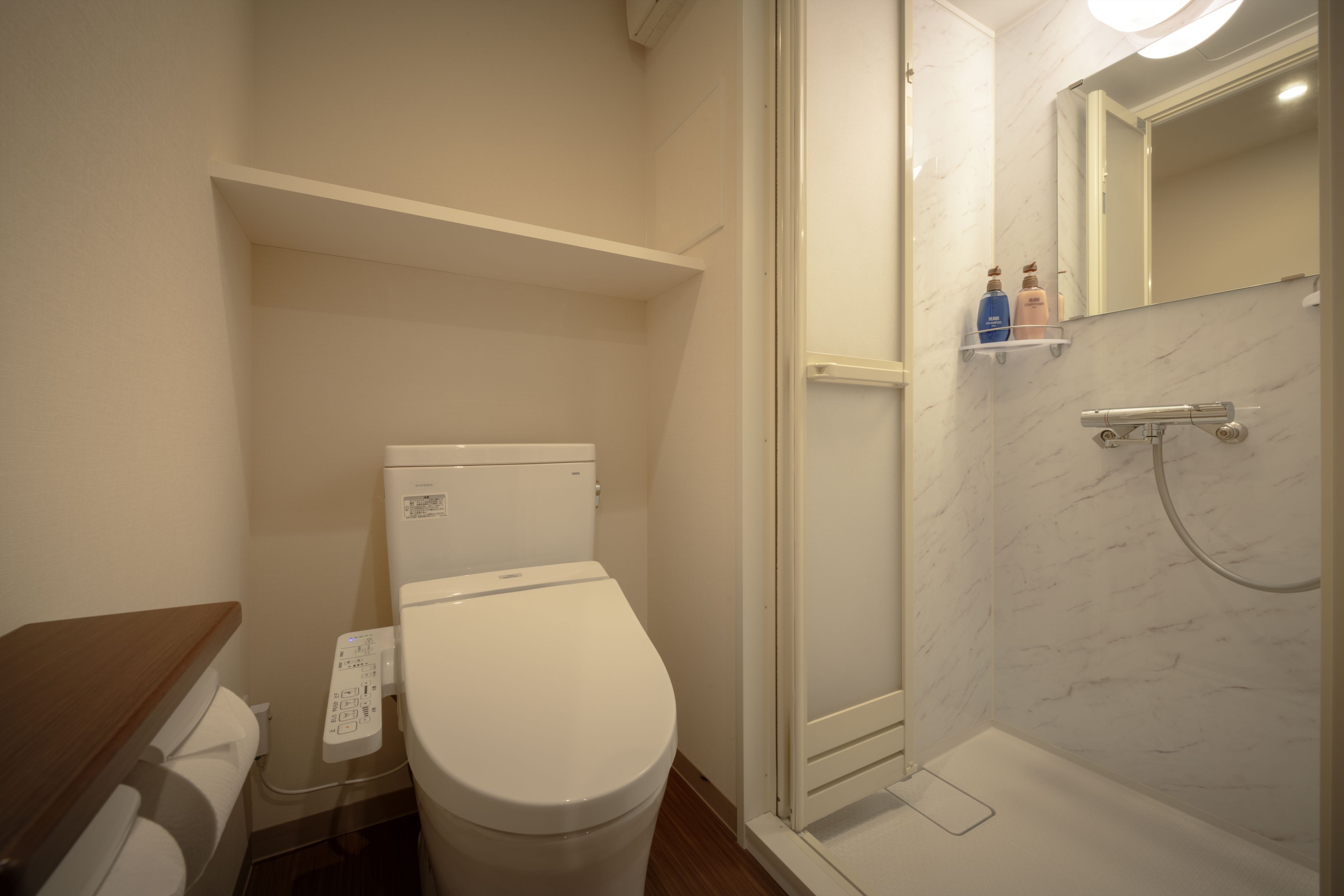 Une salle de bain avec des toilettes, une douche et un miroir. Il y a deux bouteilles sur l’étagère au-dessus du miroir.
