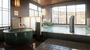 Un onsen japonés tradicional con un gran manantial termal, suelo de madera y vistas al exterior a través de amplias ventanas.