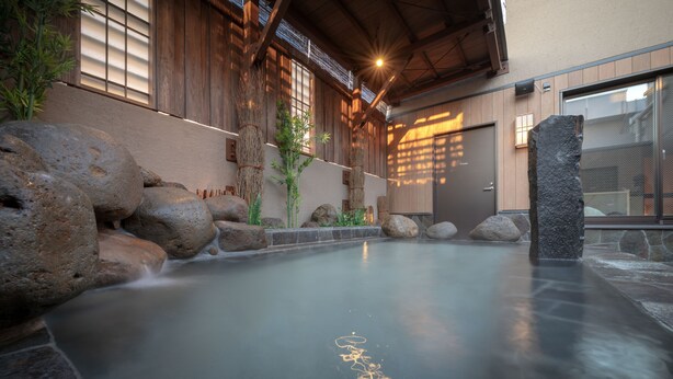Un onsen japonés tradicional con una bañera de piedra, paredes de madera y vistas al exterior.
