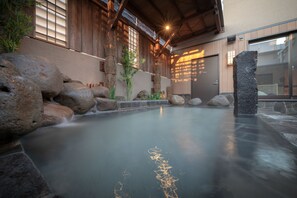A traditional Japanese onsen with a stone bath, wooden walls, and a view of the outside.