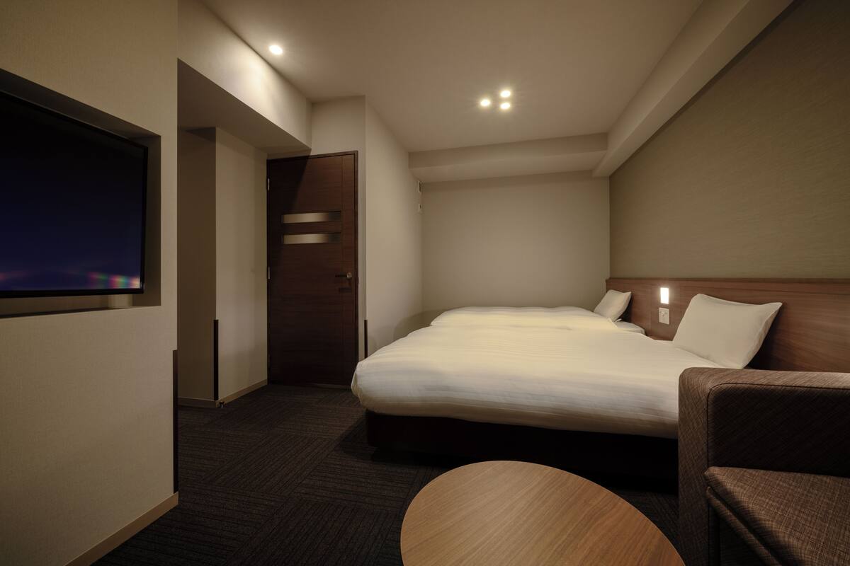 Habitación de hotel con una cama grande, un televisor montado en la pared, un cabecero de madera y una mesita redonda.