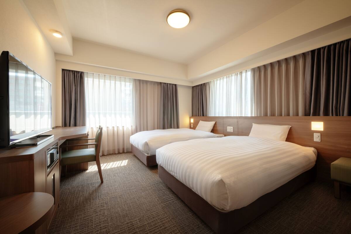 Habitación de hotel con dos camas, un escritorio, una silla y un televisor.