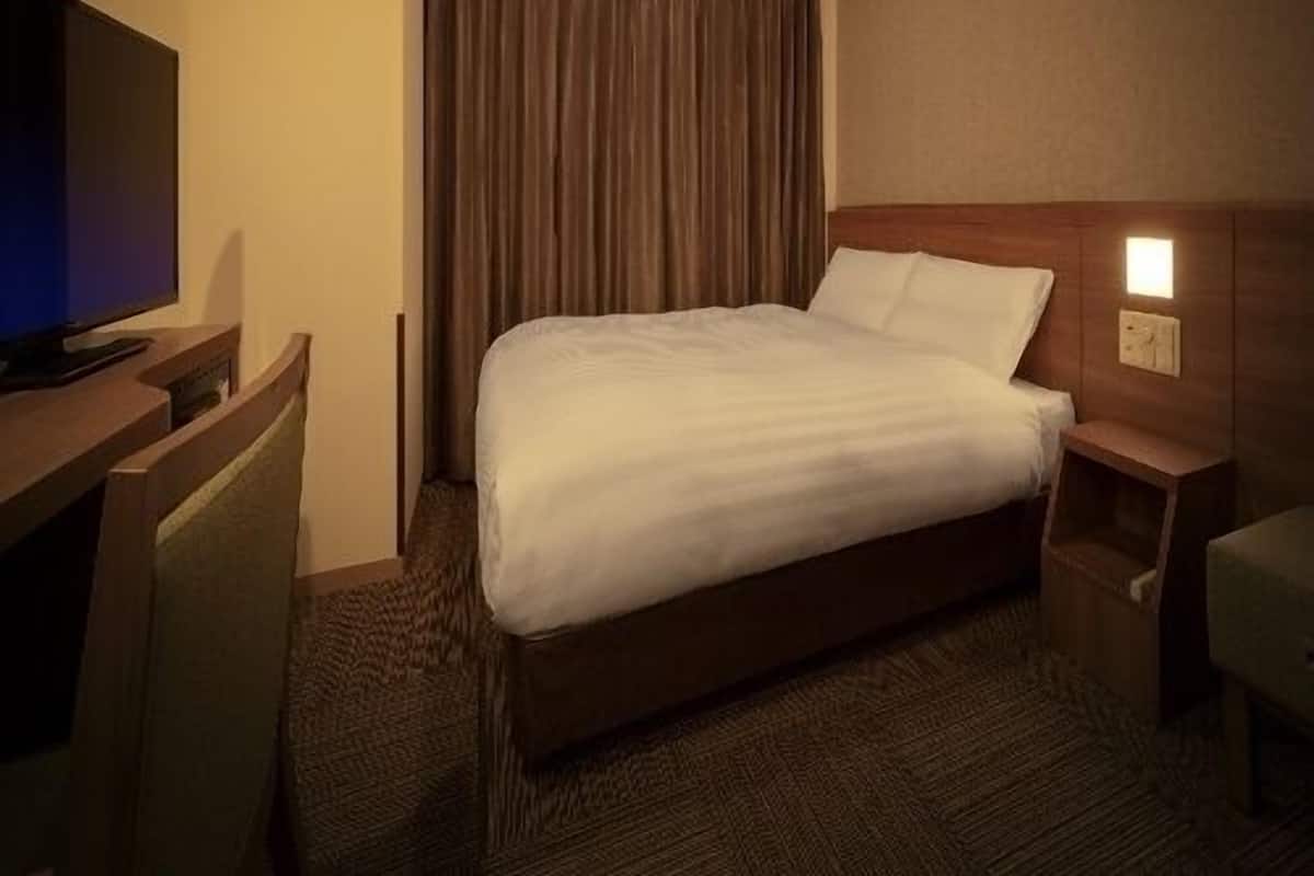 Habitación de hotel con cama, escritorio con televisor, mesita de noche y reloj de pared.