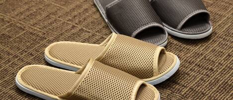 A pair of beige and gray slippers on a textured brown carpet.