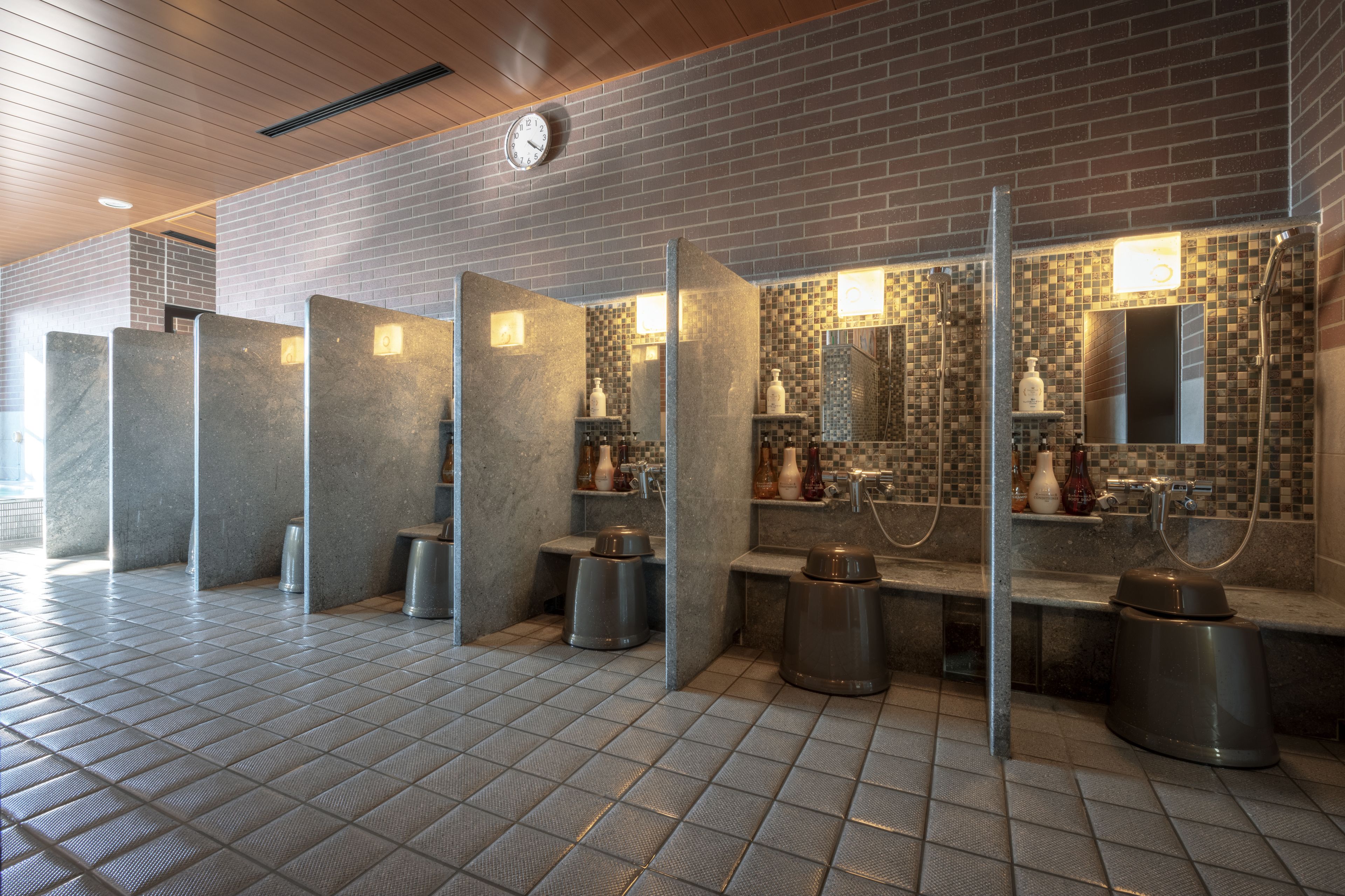 A public restroom with multiple stalls, a clock, and tiled walls.