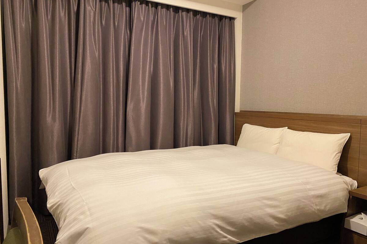 Una habitación de hotel con una cama grande, un cabecero de madera, una mesita de noche y una cortina.