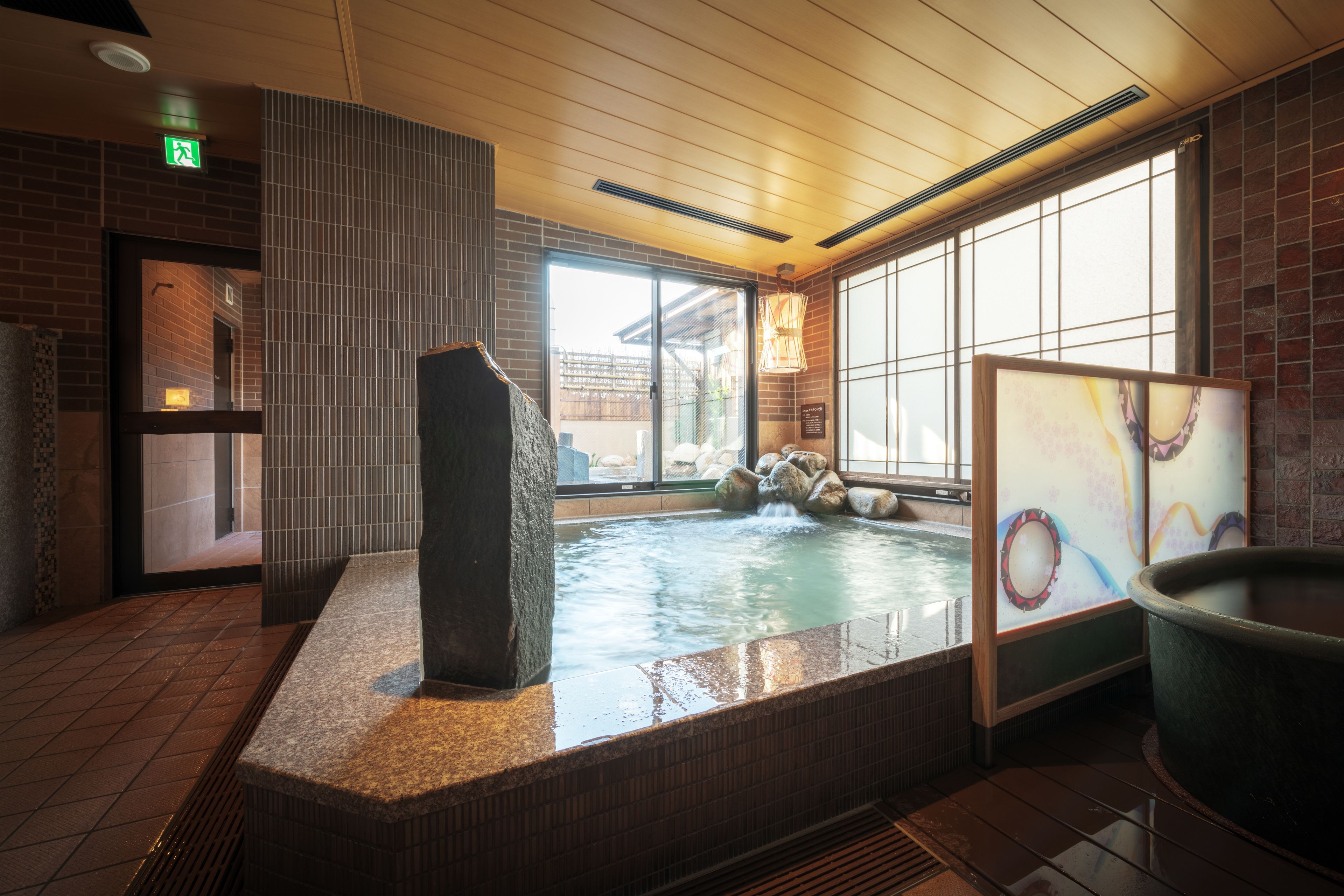 Un espace spa comprenant un bain à remous, une sculpture en pierre et une vue sur l’extérieur grâce à de grandes fenêtres.