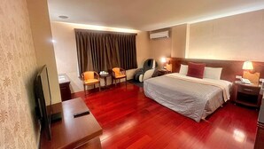 Habitación de hotel con cama, dos sillones, escritorio, televisión y ventana con cortinas.
