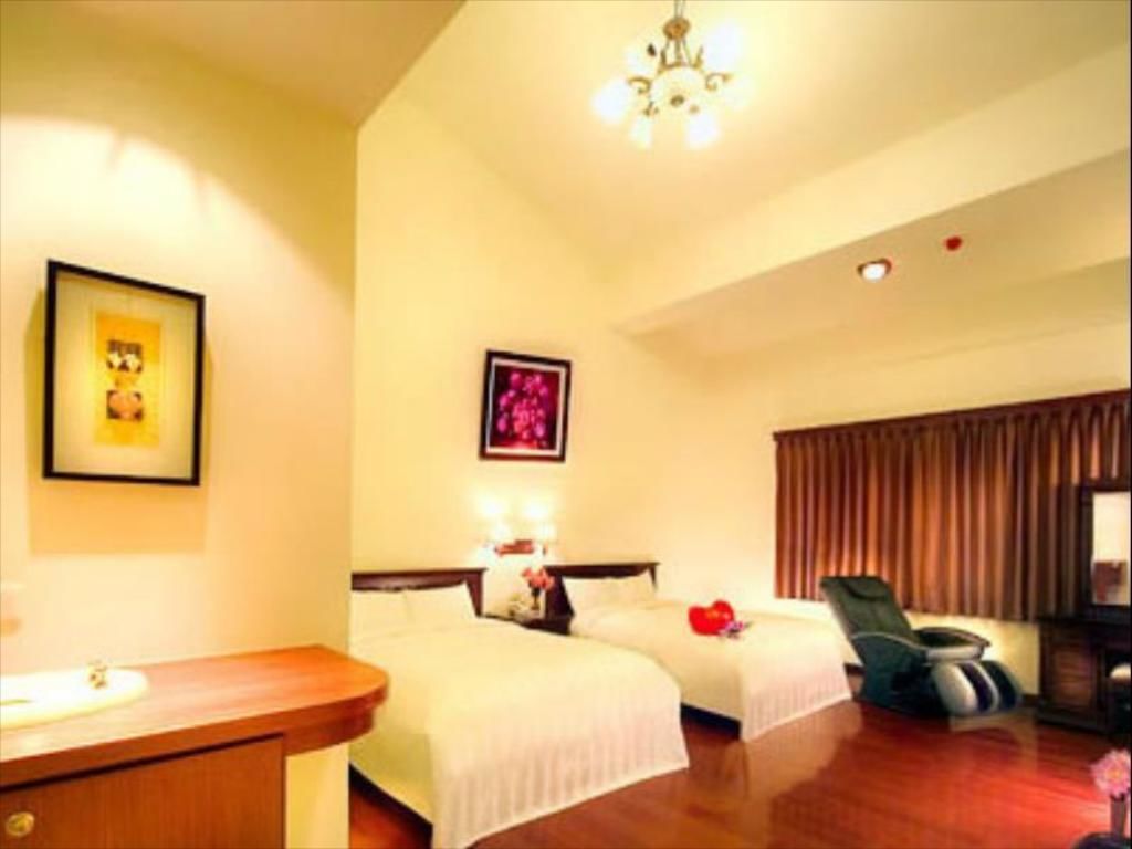 A hotel room with two beds, a desk, a chair, and a chandelier.