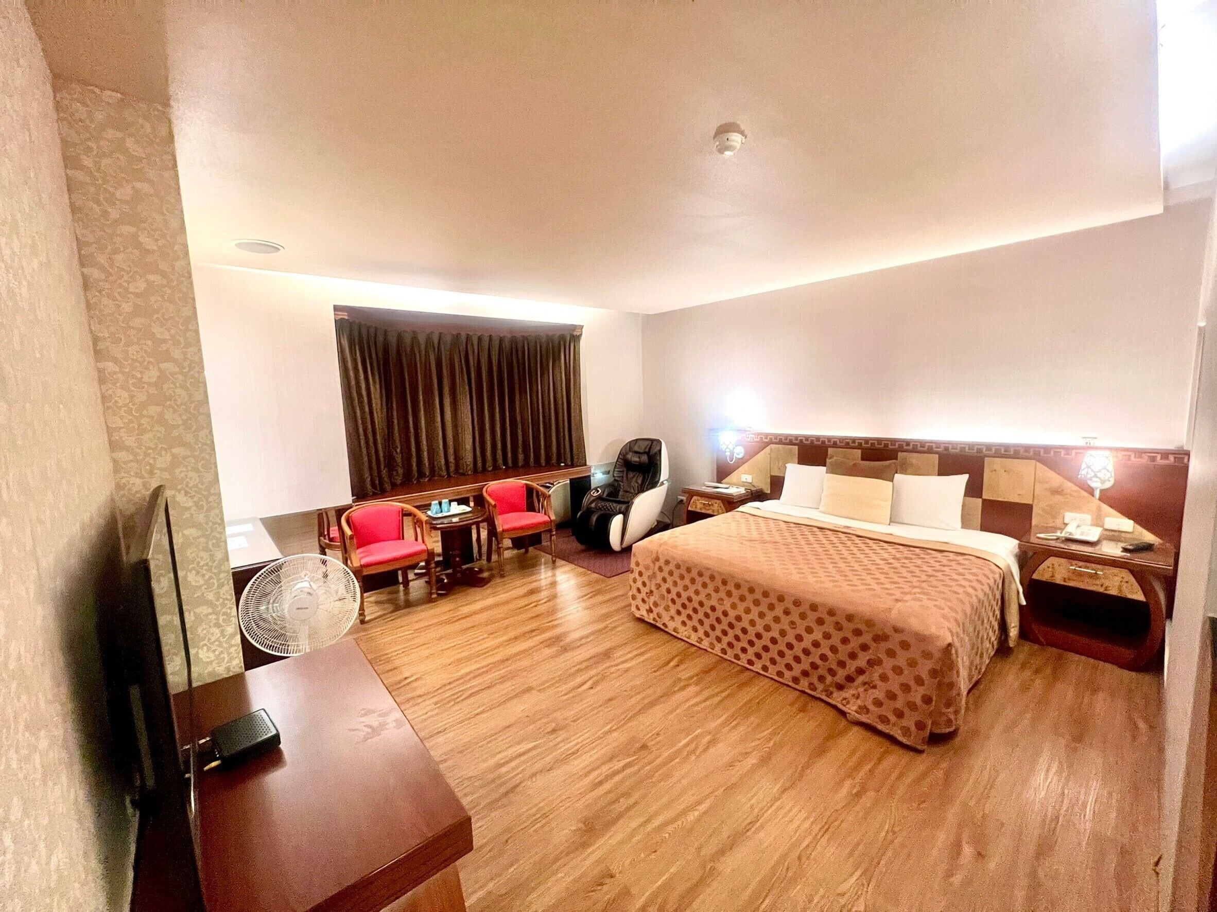 A hotel room with a bed, a desk, a chair, a sofa, and a fan.