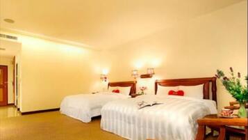 A hotel room with two beds, a wooden headboard, bedside tables with lamps, and a small table with a vase.