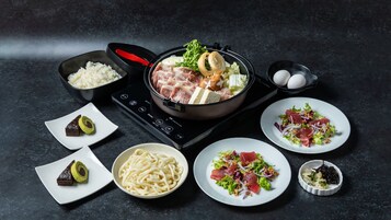 Una mesa dispuesta para comer, con una olla de comida, platos de sushi, fideos y una ensalada.