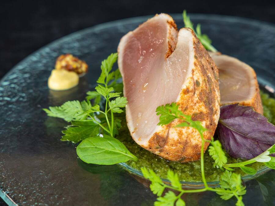 A dish with a piece of meat, greens, and a sauce on a glass plate.