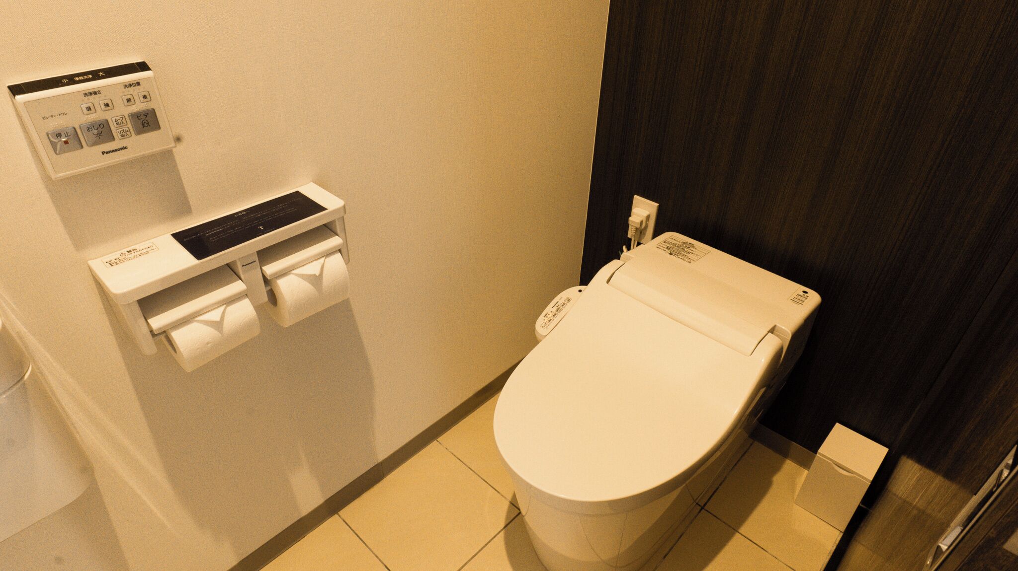 A toilet with a paper towel dispenser and a control panel above it.