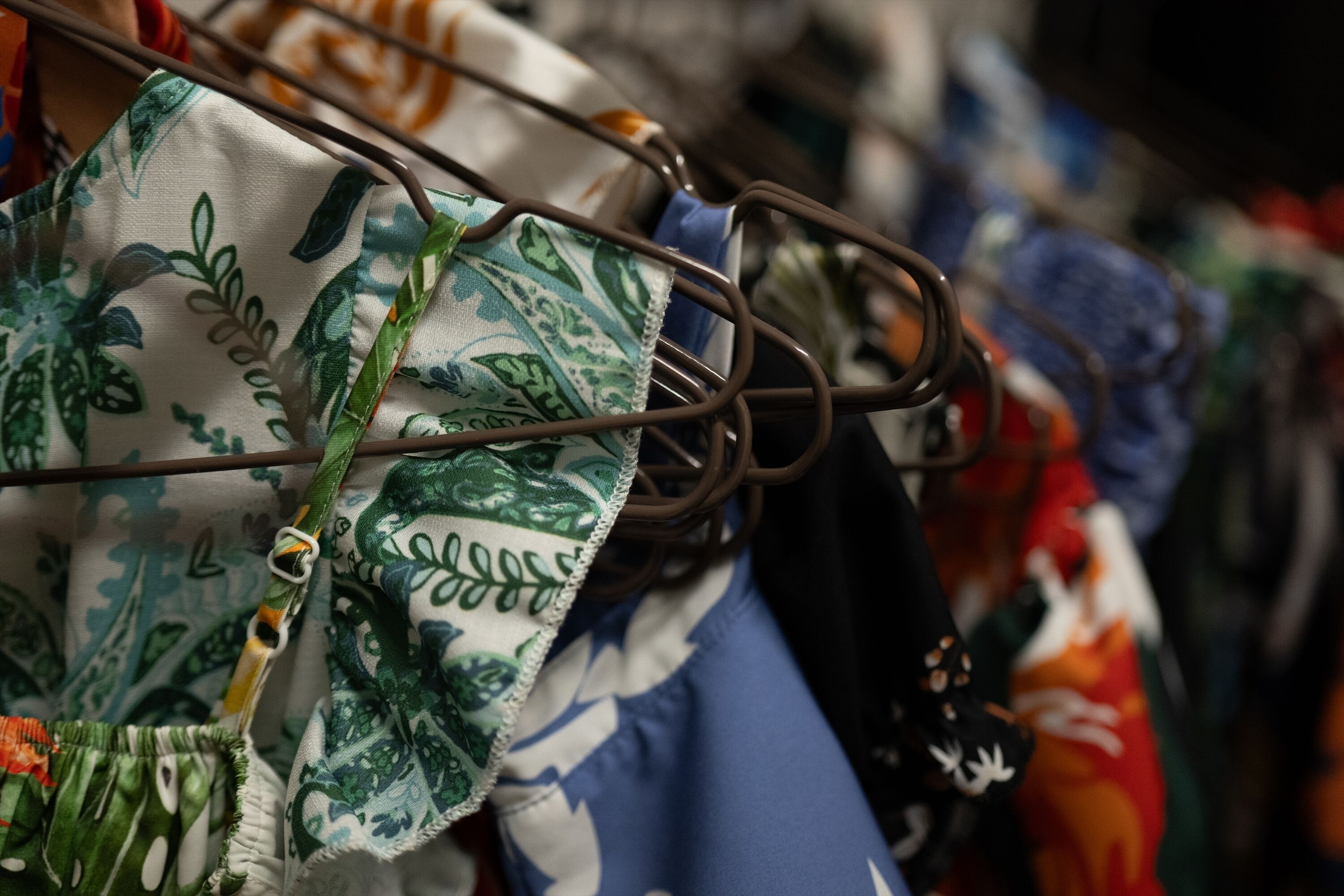 Un portant à vêtements sur lequel sont disposés divers articles, notamment un tissu à motifs verts et blancs et un vêtement bleu.