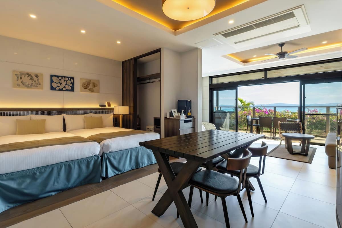 A modern hotel room with a large bed, a dining table, and a balcony with a view.