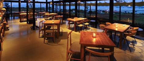 Ein geräumiges Restaurant mit Holztischen und -stühlen, großen Fenstern mit Blick ins Freie und hängenden Pendelleuchten.