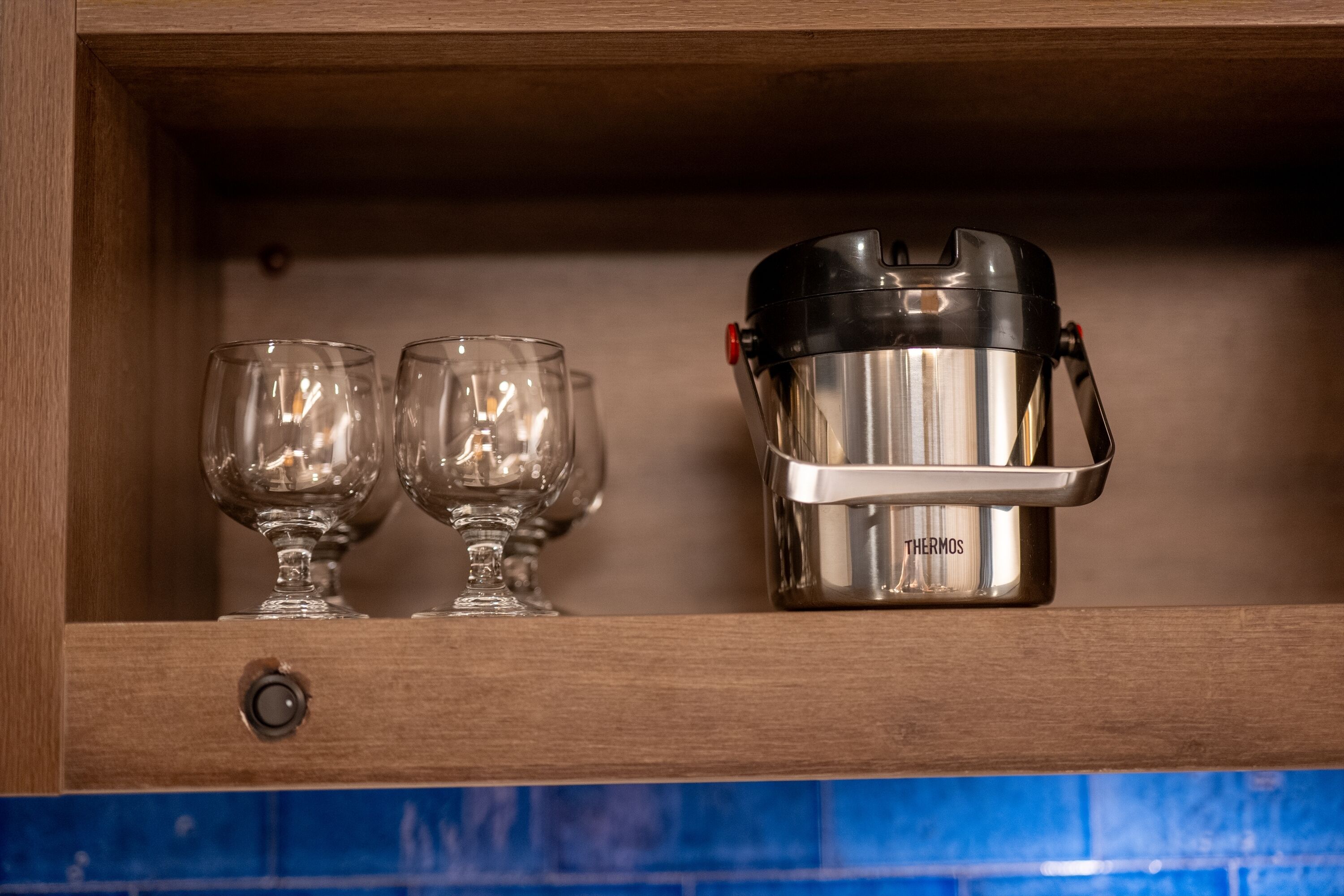 A stainless steel thermos with a red button on a wooden shelf.