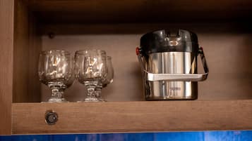 A stainless steel thermos with a red button on a wooden shelf.