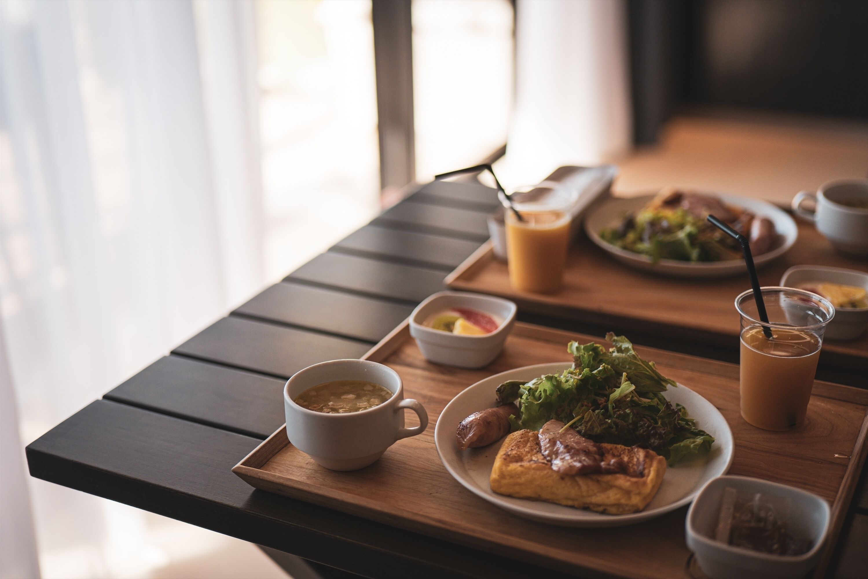 Un plateau de petit-déjeuner avec une tasse de café, un bol de soupe, une assiette d’œufs, des toasts et un verre de café glacé.