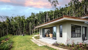 Et moderne hus med en overdækket terrasse, omgivet af frodigt grønt og høje træer.