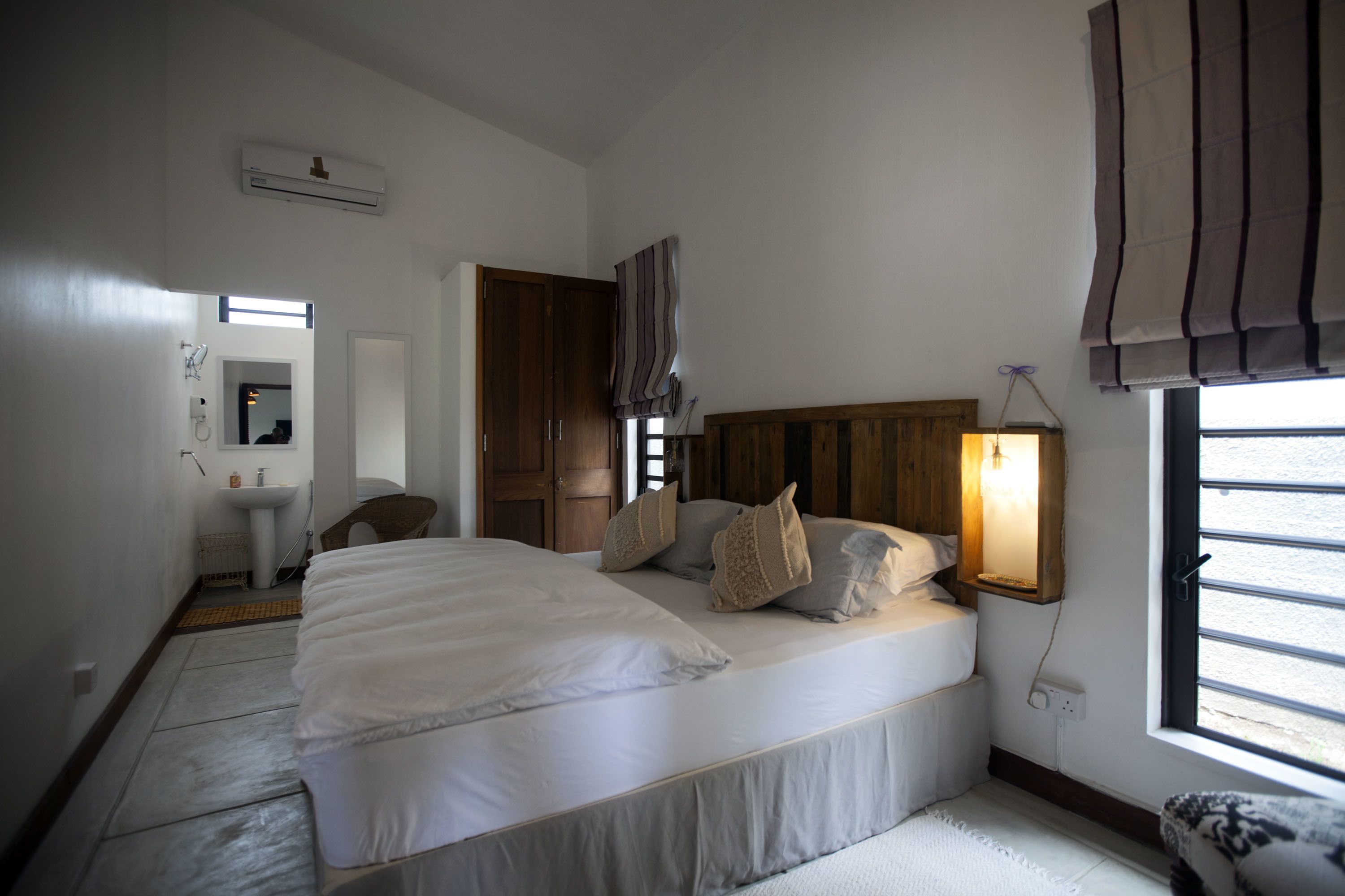 A bedroom with a large bed, a bedside table, a hanging light, and a window with curtains.