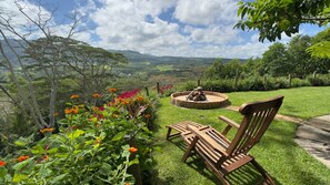 A wooden bench and a fire pit in a grassy garden with a view of a valley and mountains. - Green Cottage Chamarel (Chamarel)